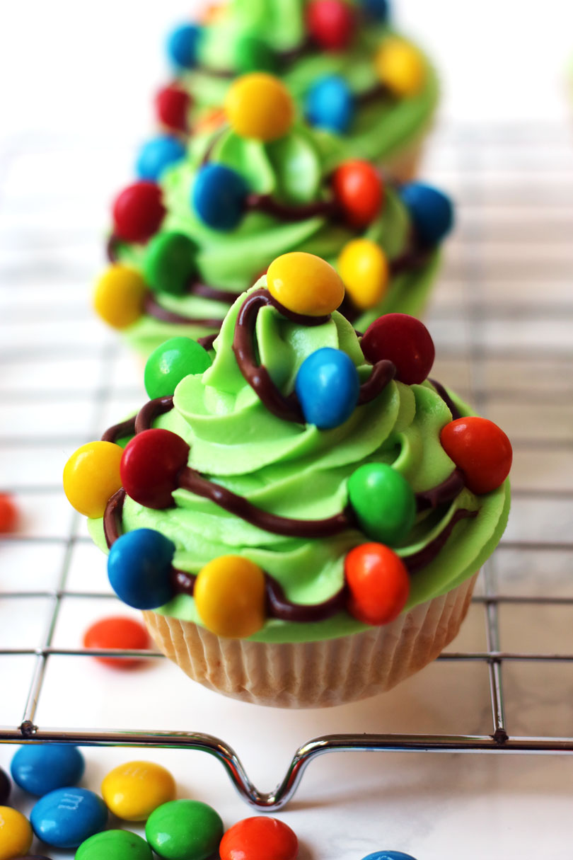 Christmas Tree Cupcakes are made with a vanilla sponge, bright green buttercream icing and chocolate swirls with M&Ms for fairy lights.