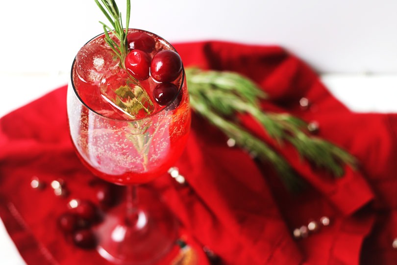 A single glass of Cranberry and Aperol Spritz, a Christmas Cocktail garnished with fresh cranberries and rosemary.