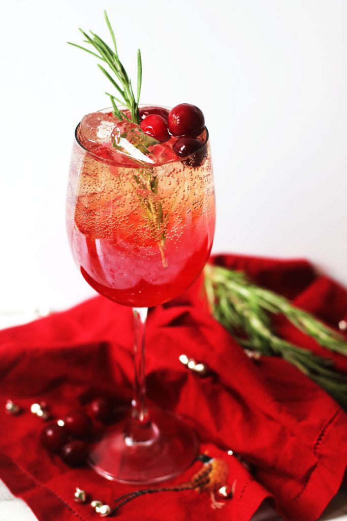 Cranberry and Aperol Spritz, a single wine glass of Christmas cocktail, garnished with fresh cranberries, rosemary and served over ice.