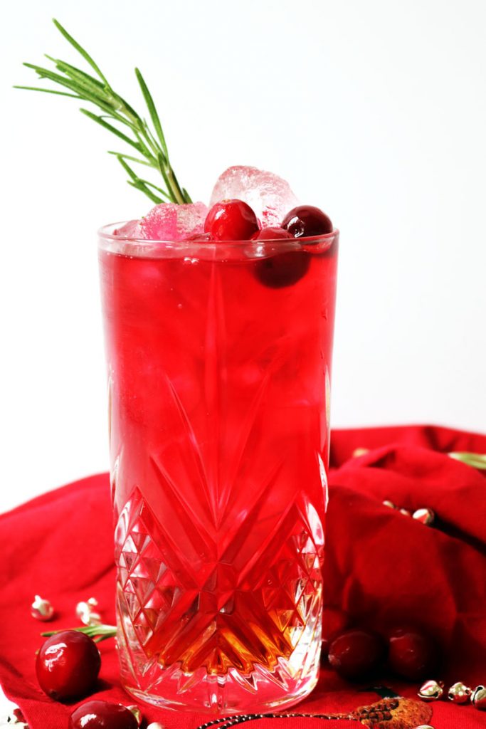 A long, tall glaas of cranberry juice and amaretto served over ice and garnished with fresh cranberries and rosemary