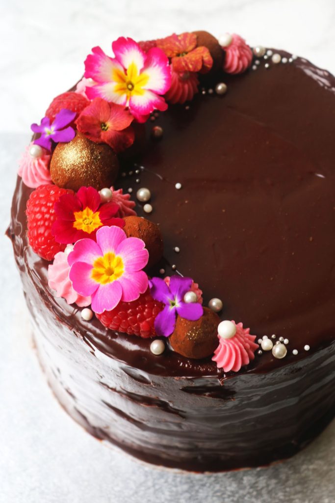 Cake covered in chocolate ganache and topped with truffles, rasbperries and edible flowers 2