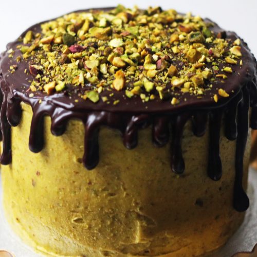 Chocolate and Pistachio Cake on a gold cake stand with chocolate ganache drips and chopped pistachios