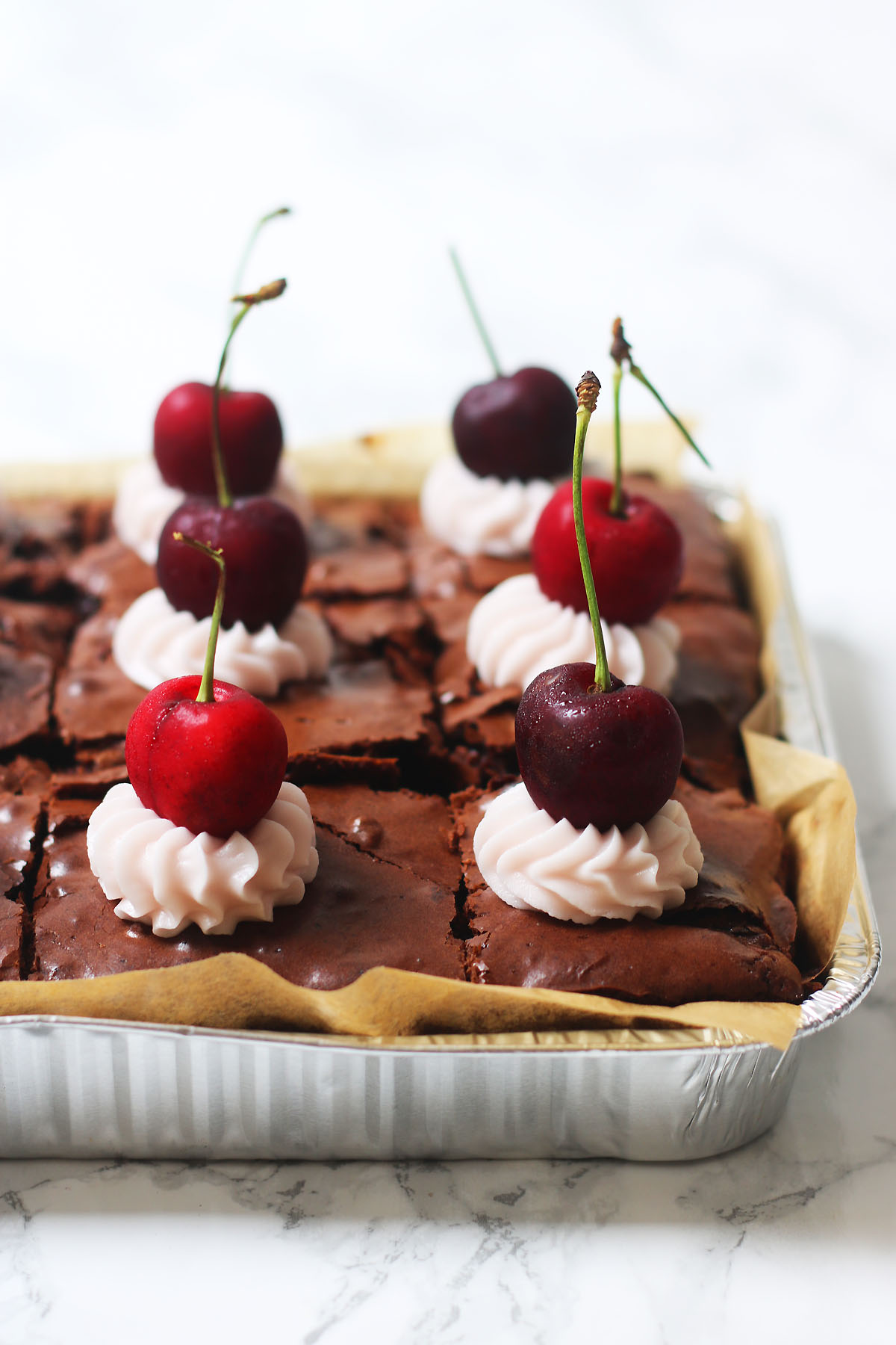 A tray of cherry and pecan brownies topped with cherry buttercream and fresh cherries