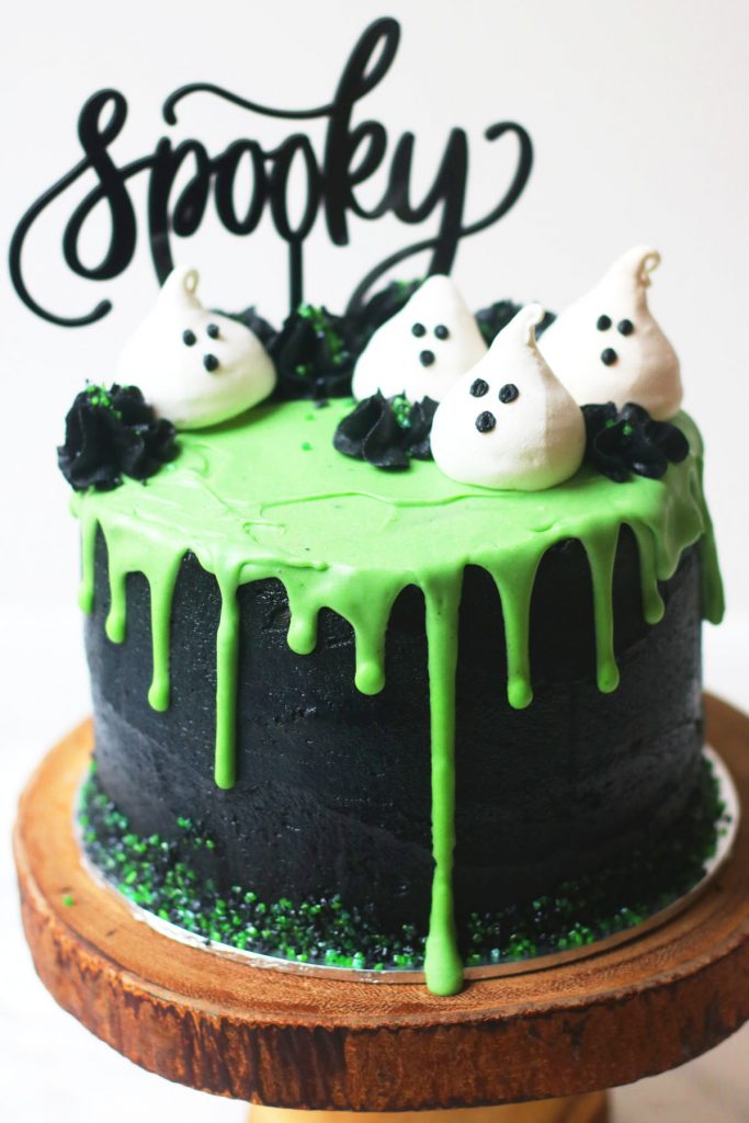 Halloween layer cake: Coconut and Lime Slime Cake. Decorated with black buttercream and green white chocolate ganache drip and coconut meringue ghosts.