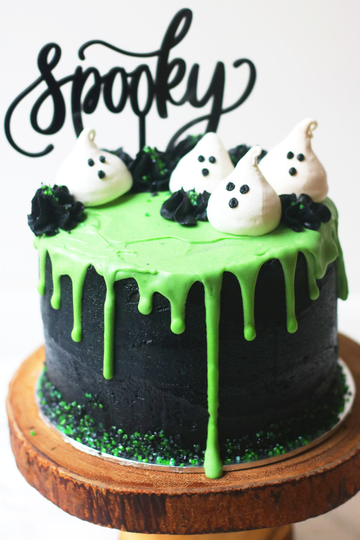 Halloween layer cake: Coconut and Lime Slime Cake. Decorated with black buttercream and green white chocolate ganache drip and coconut meringue ghosts.