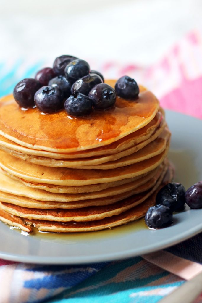 A large stack of vegan American style pancakes with maple syrup and blueberries