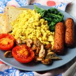 A plate of toast, grilled tomatoes, sauteed mushrooms, spinach, vegetarian sausages and tofu scramble