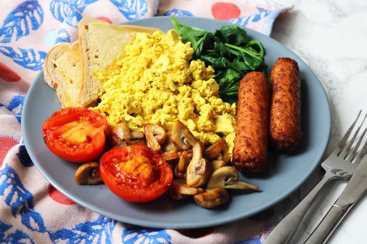 A plate of toast, grilled tomatoes, sauteed mushrooms, spinach, vegetarian sausages and tofu scramble