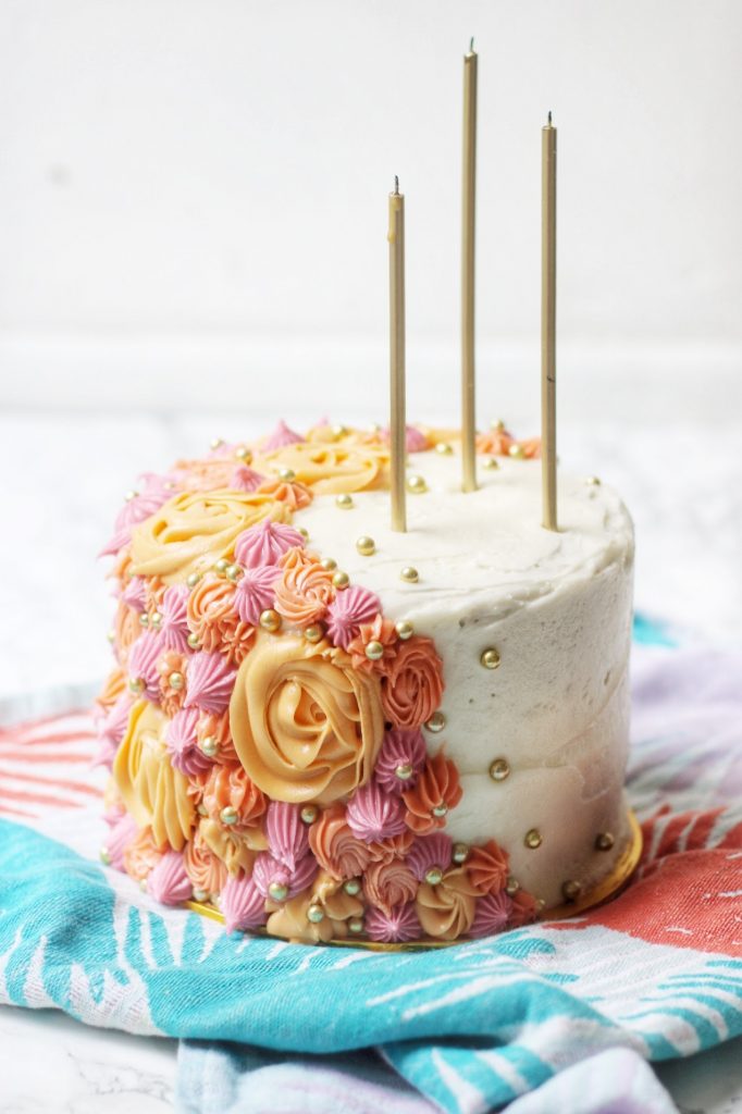 A Vegan Carrot Cake decorated with piped flowers and tall gold candles