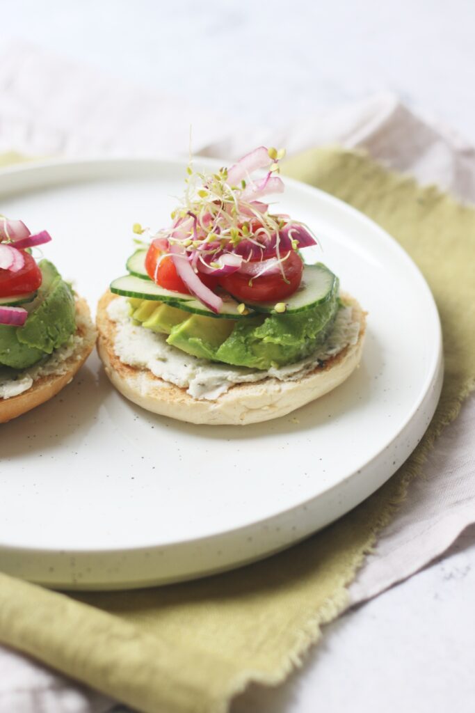 Vegan Cream Cheese and Avocado Bagels topped with cucumber, tomatoes, pickled red onions and alfalfa sprouts