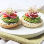 Vegan Cream Cheese and Avocado Bagels topped with cucumber, tomatoes, pickled red onions and alfalfa sprouts