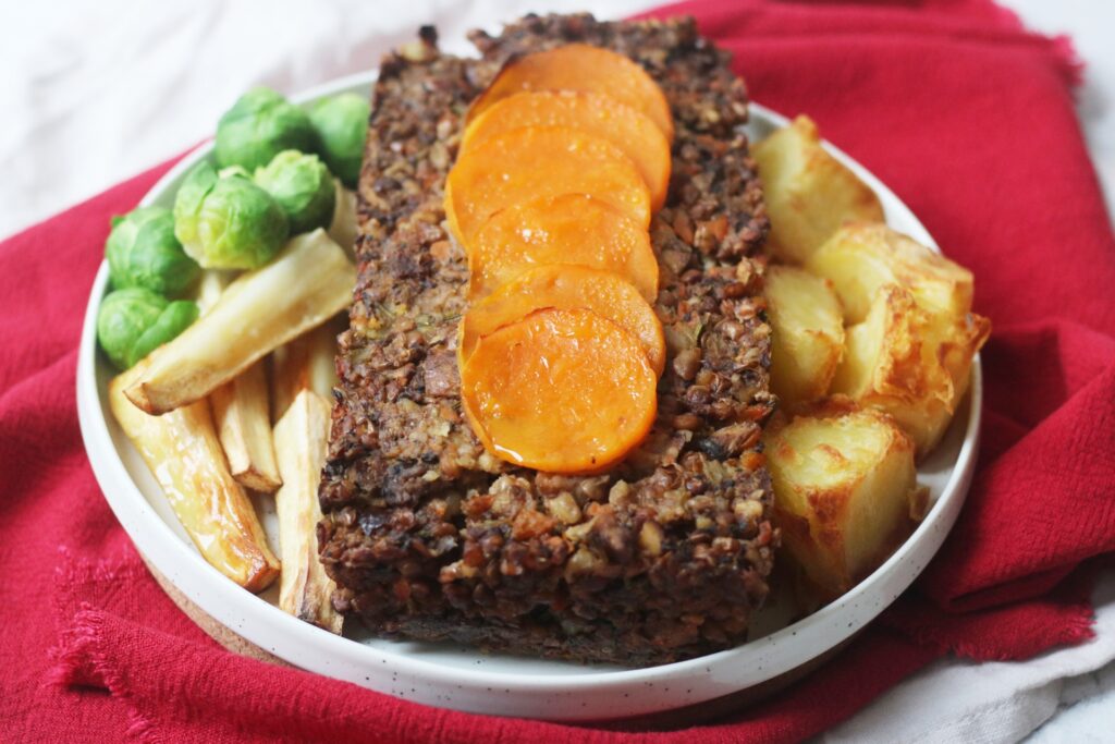 Vegan Butternut Squash Nut Roast topped with butternut squash circles and served with parsnips, brussels sprouts and roast potatoes