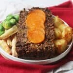 Vegan Butternut Squash Nut Roast topped with butternut squash circles and served with parsnips, brussels sprouts and roast potatoes