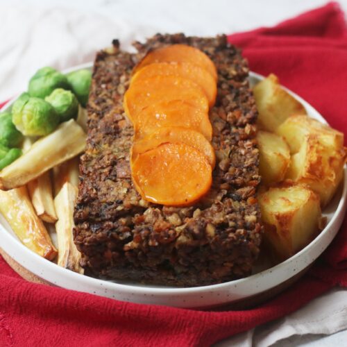 Vegan Butternut Squash Nut Roast topped with butternut squash circles and served with parsnips, brussels sprouts and roast potatoes