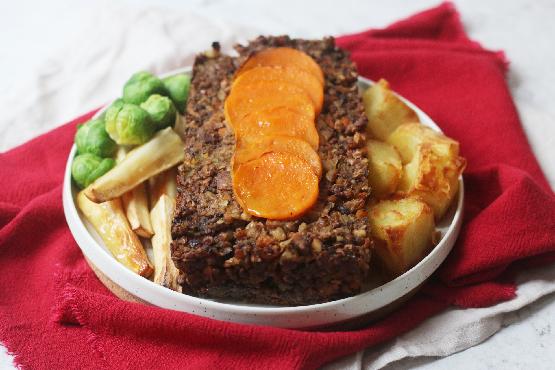 Vegan Butternut Squash Nut Roast topped with butternut squash circles and served with parsnips, brussels sprouts and roast potatoes