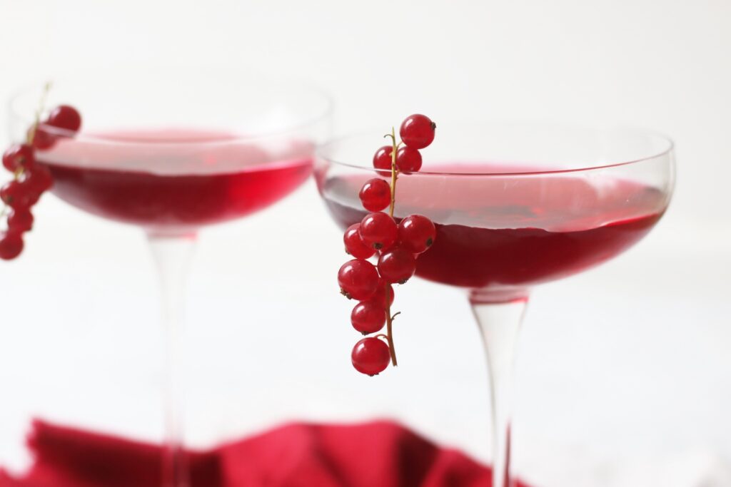 Two martini glasses of a Redcurrant Cosmopolitan Cocktail with redcurrants garnishing the glass