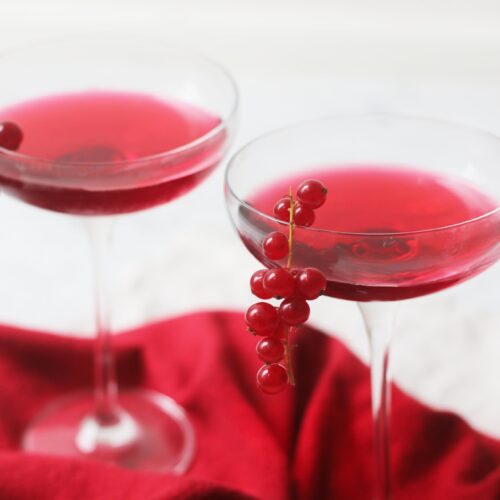 Two martini glasses of a Redcurrant Cosmopolitan Cocktail with redcurrants garnishing the glass