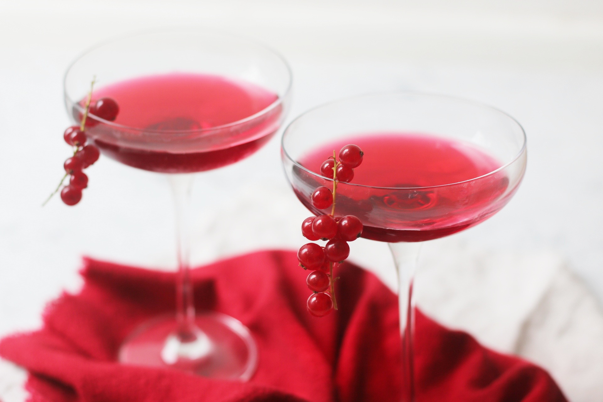 Two martini glasses of a Redcurrant Cosmopolitan Cocktail with redcurrants garnishing the glass