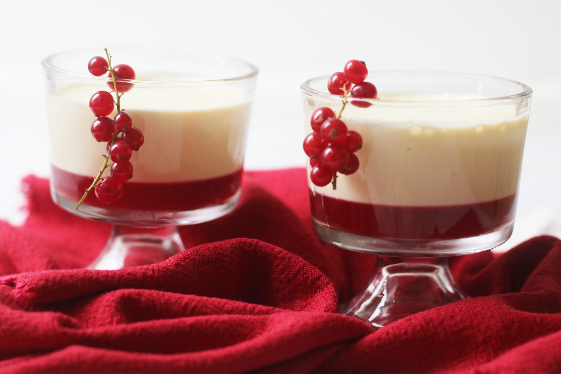 Two pudding glasses filled with a redcurrant jelly topped with an orange posset. Redcurrants garnish the dessert.