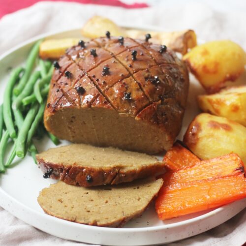 Vegan Seitan Roast Ham Joint on a plate with roasted vegetables