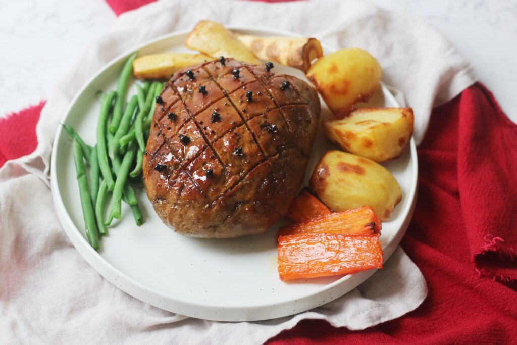 Vegan Seitan Roast Ham Joint on a plate with roasted vegetables