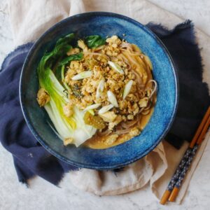 A bowl of vegan dan dan noodles and chopsticks on a blue and cream napkin