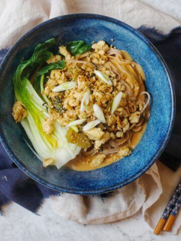 A bowl of vegan dan dan noodles and chopsticks on a blue and cream napkin