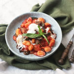 Vegan Baked Gnocchi topped with basil and served on a blue plate