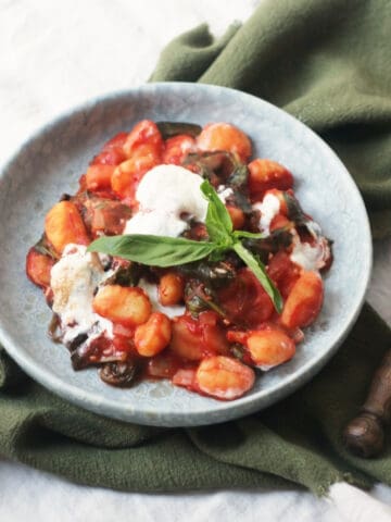 Vegan Baked Gnocchi topped with basil and served on a blue plate