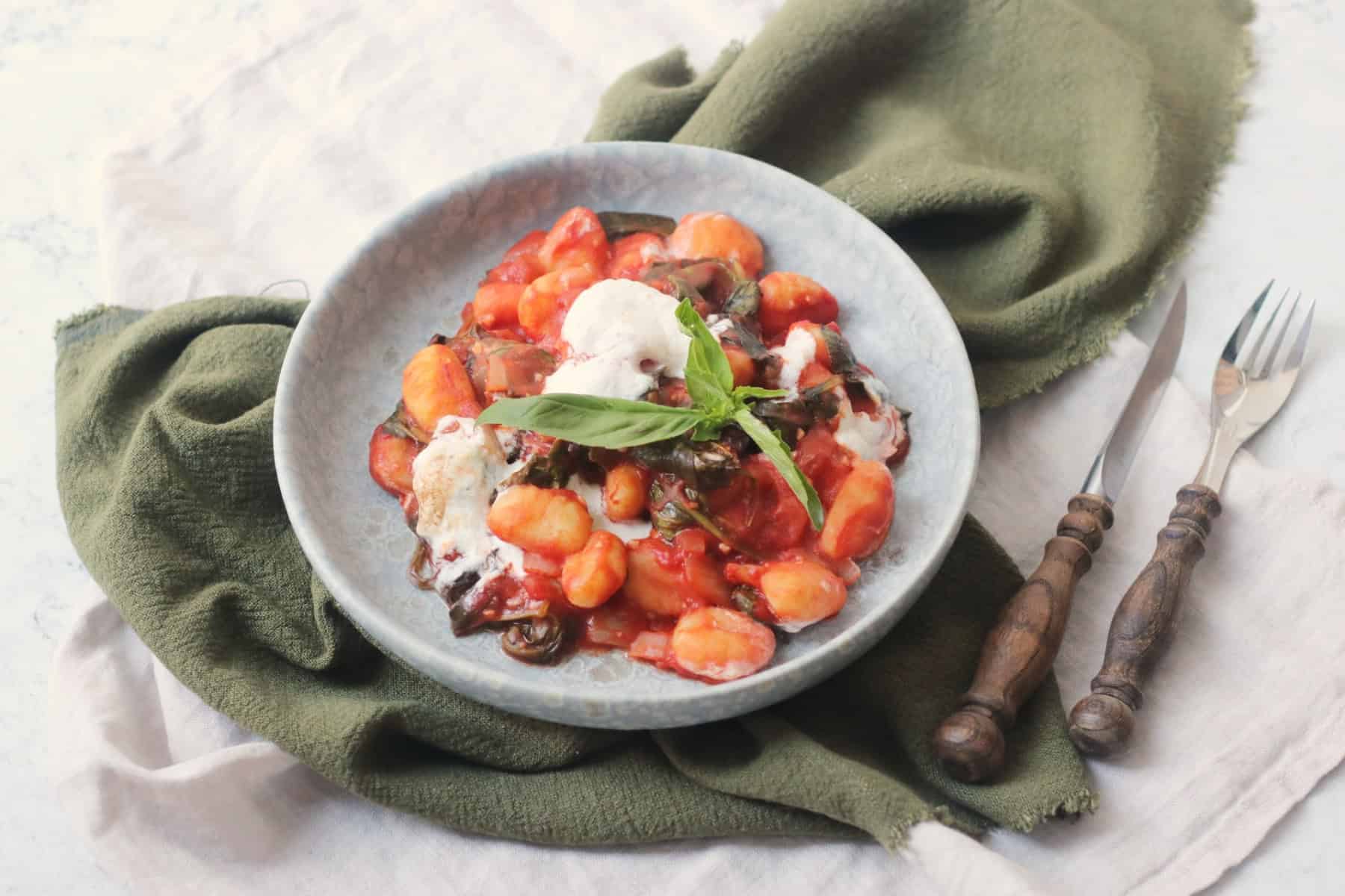 Vegan Baked Gnocchi topped with basil and served on a blue plate