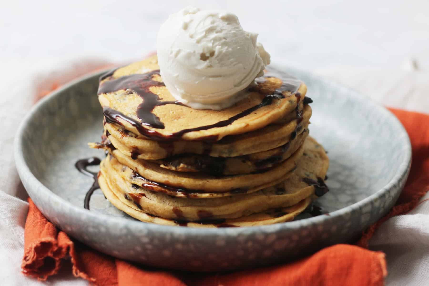 A stack of Vegan Sweet Potato Pancakes with chocolate sauce and ice cream