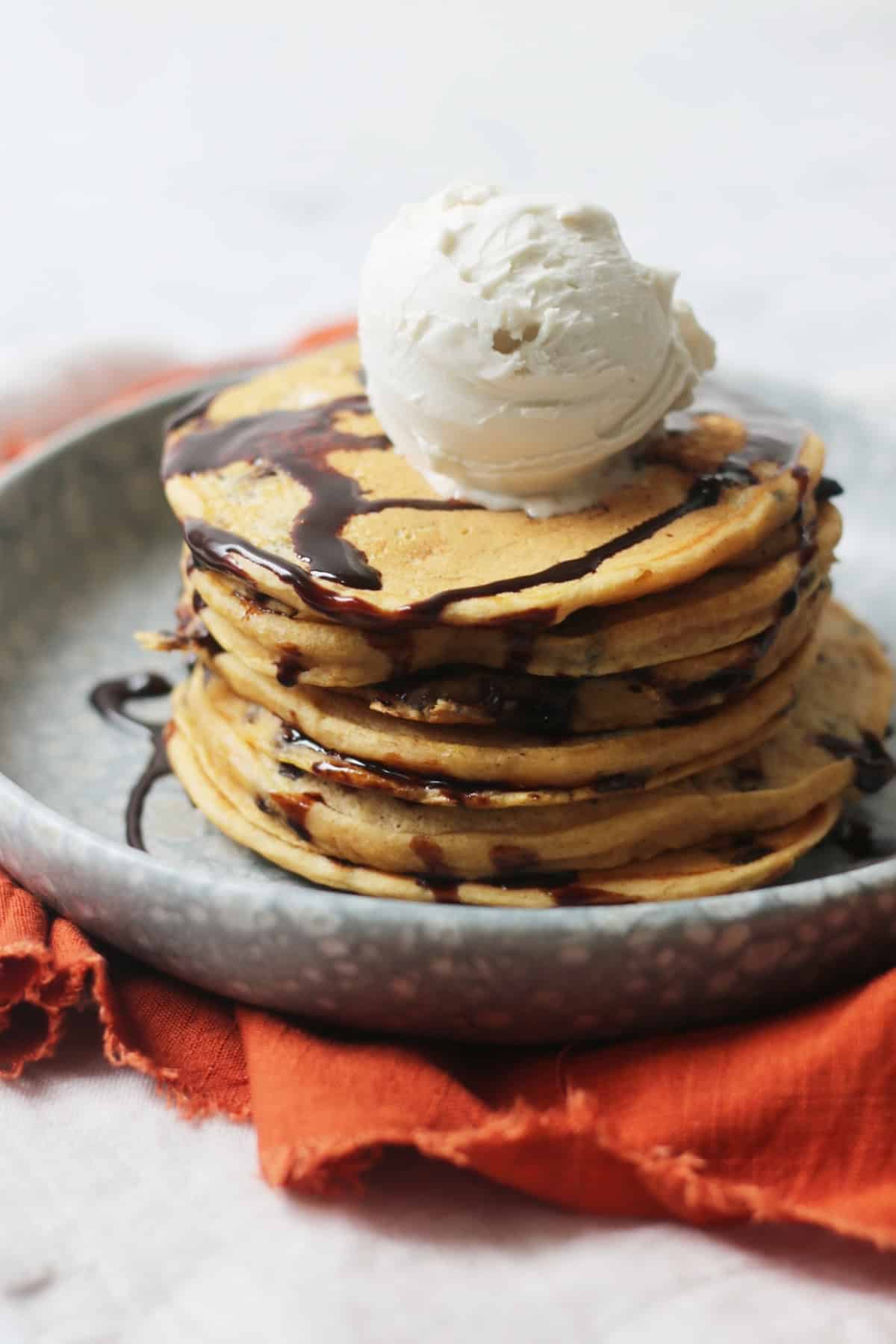 A close up of a stack of Vegan Sweet Potato Pancakes with chocolate sauce