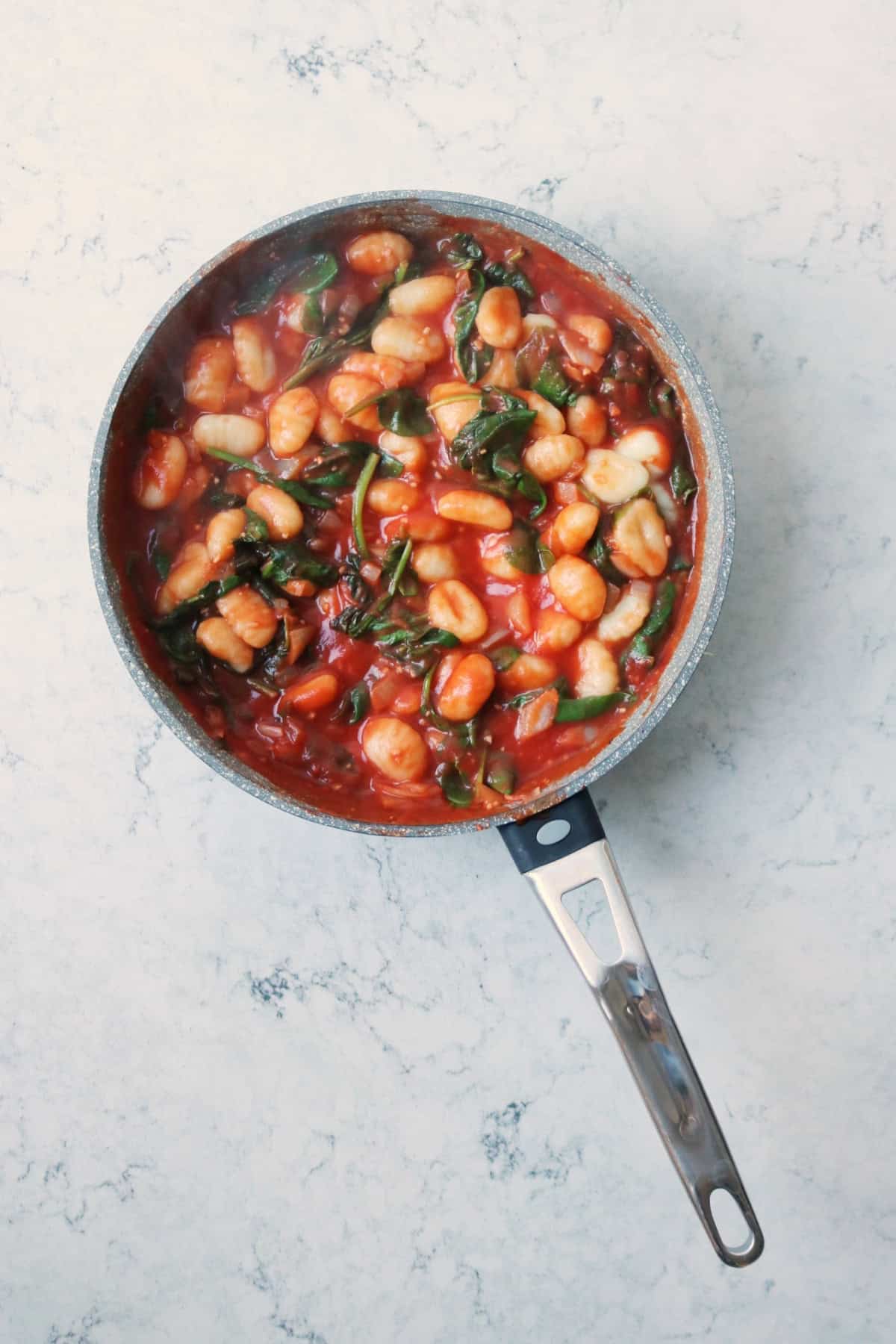 Gnocchi and wilted spinach in tomato sauce in a sauce pan