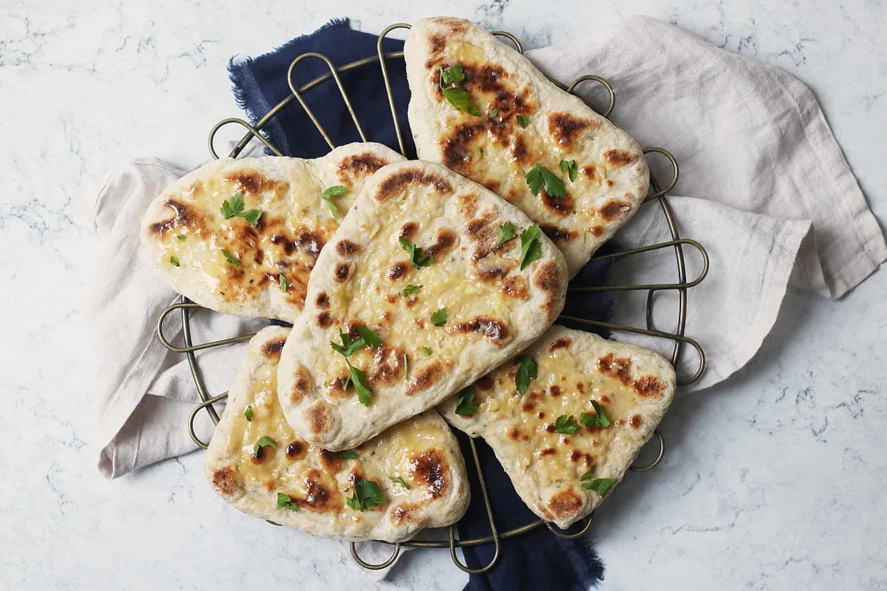 An overhead shot of 5 vegan naan breads stacked on top of a wire rack