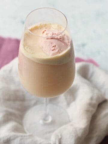 A wine glass filled with vegan raspberry ice cream and topped with champagne to make a vegan raspberry champagne float.