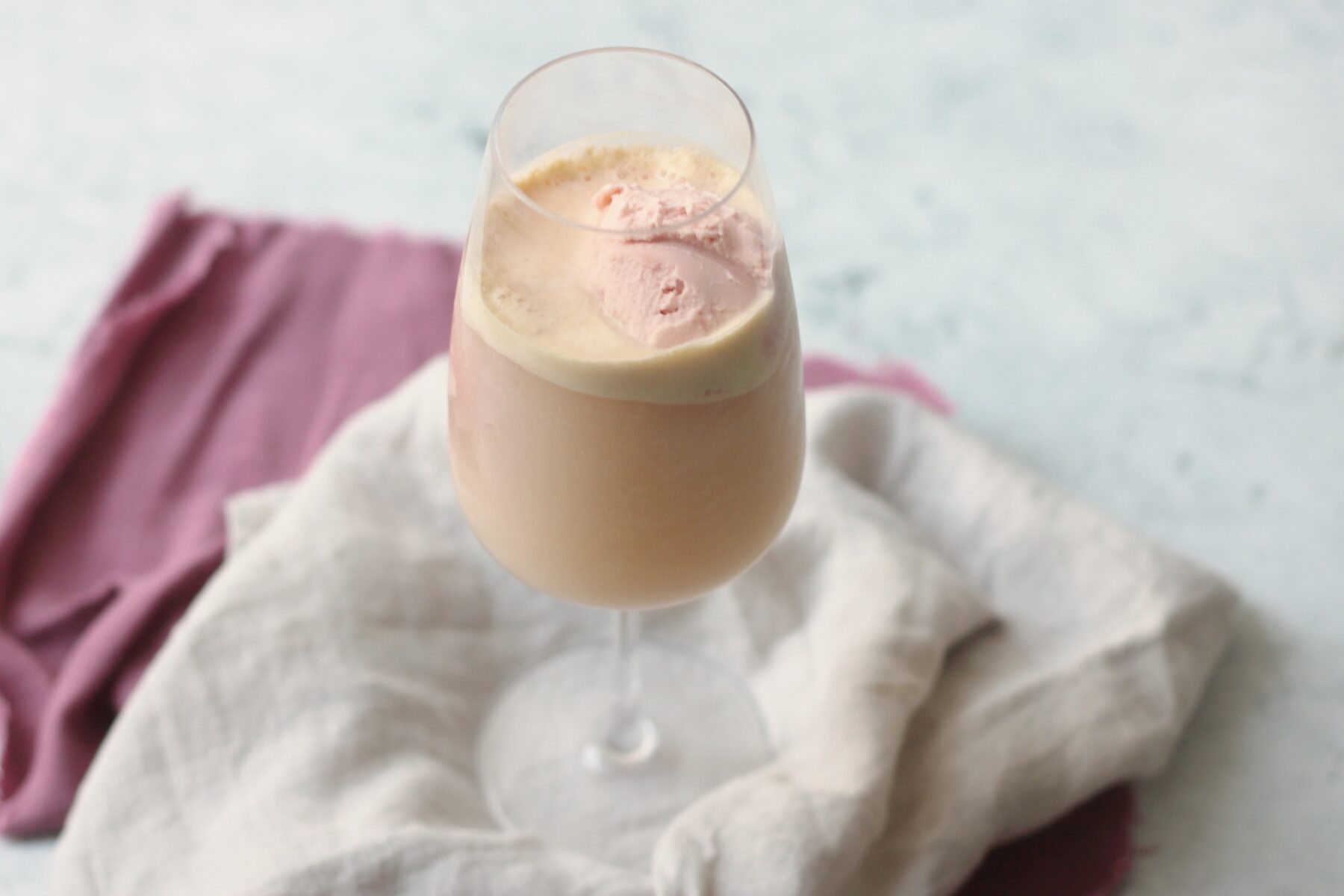 A wine glass filled with vegan raspberry ice cream and topped with champagne to make a vegan raspberry champagne float.