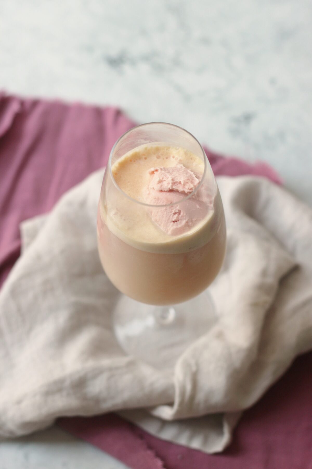 A wine glass filled with vegan raspberry ice cream and topped with champagne to make a vegan raspberry champagne float.