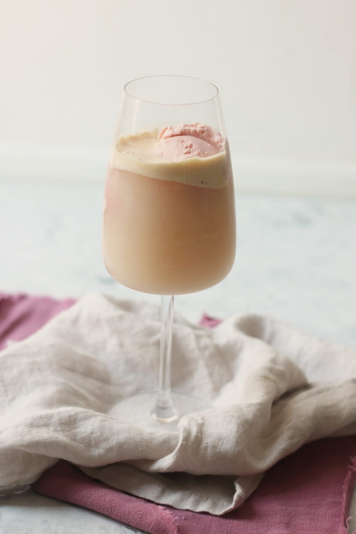 A wine glass filled with vegan raspberry ice cream and topped with champagne to make a vegan raspberry champagne float.