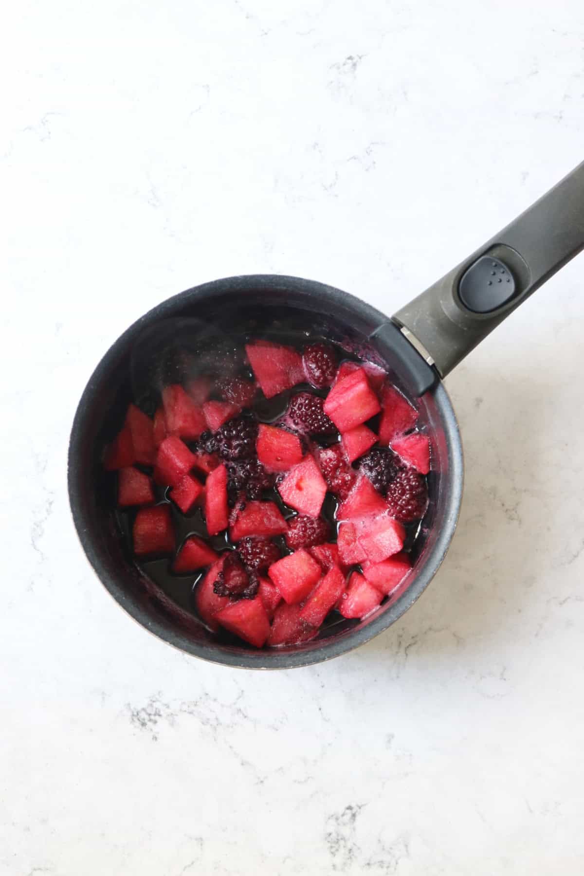 Stewed blackberries and diced apple in a black saucepan