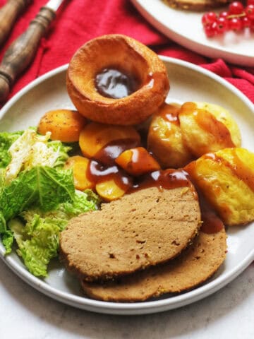 A plate of vegan roast beef with cabbage, roast potatoes, carrots a vegan Yorkshire pudding and a thick gravy.