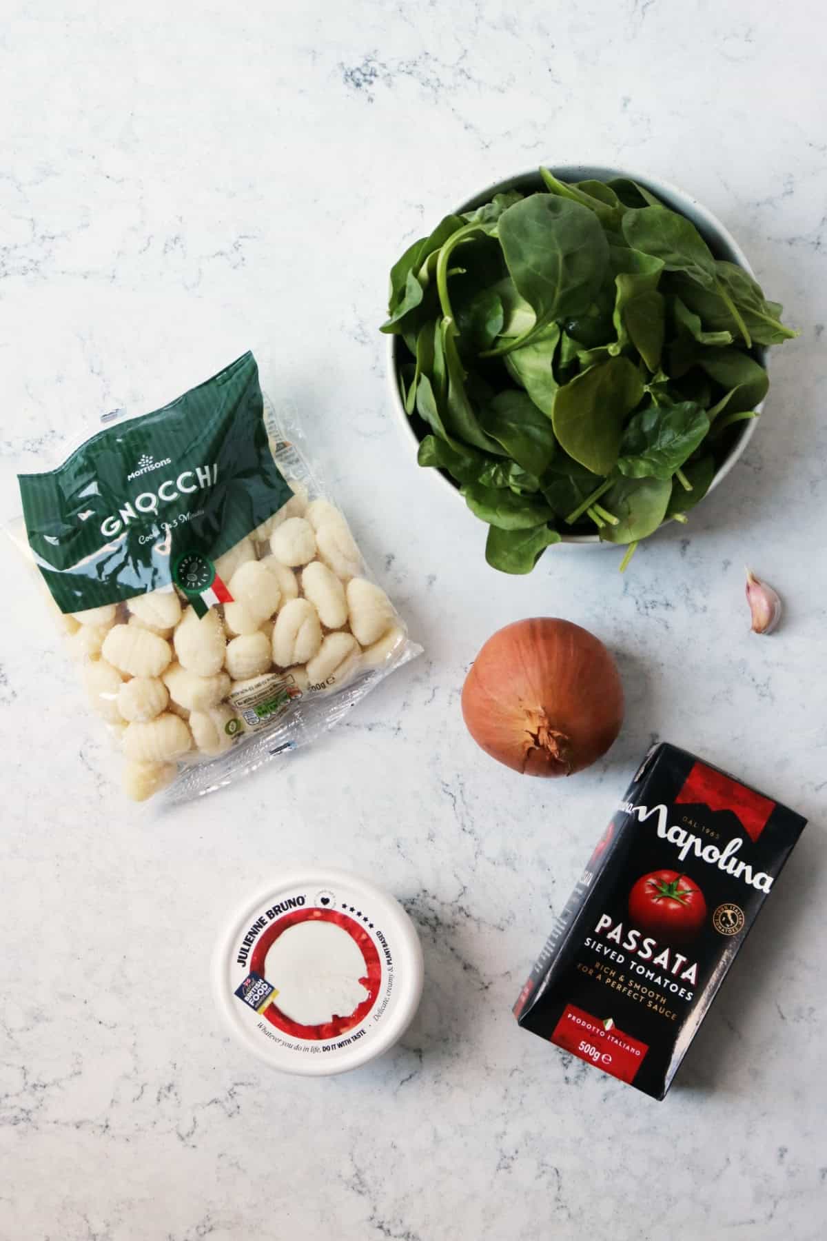 Spinach, gnocchi, white onion, two garlic cloves, vegan mozzarella and a carton of passata on a white counter top