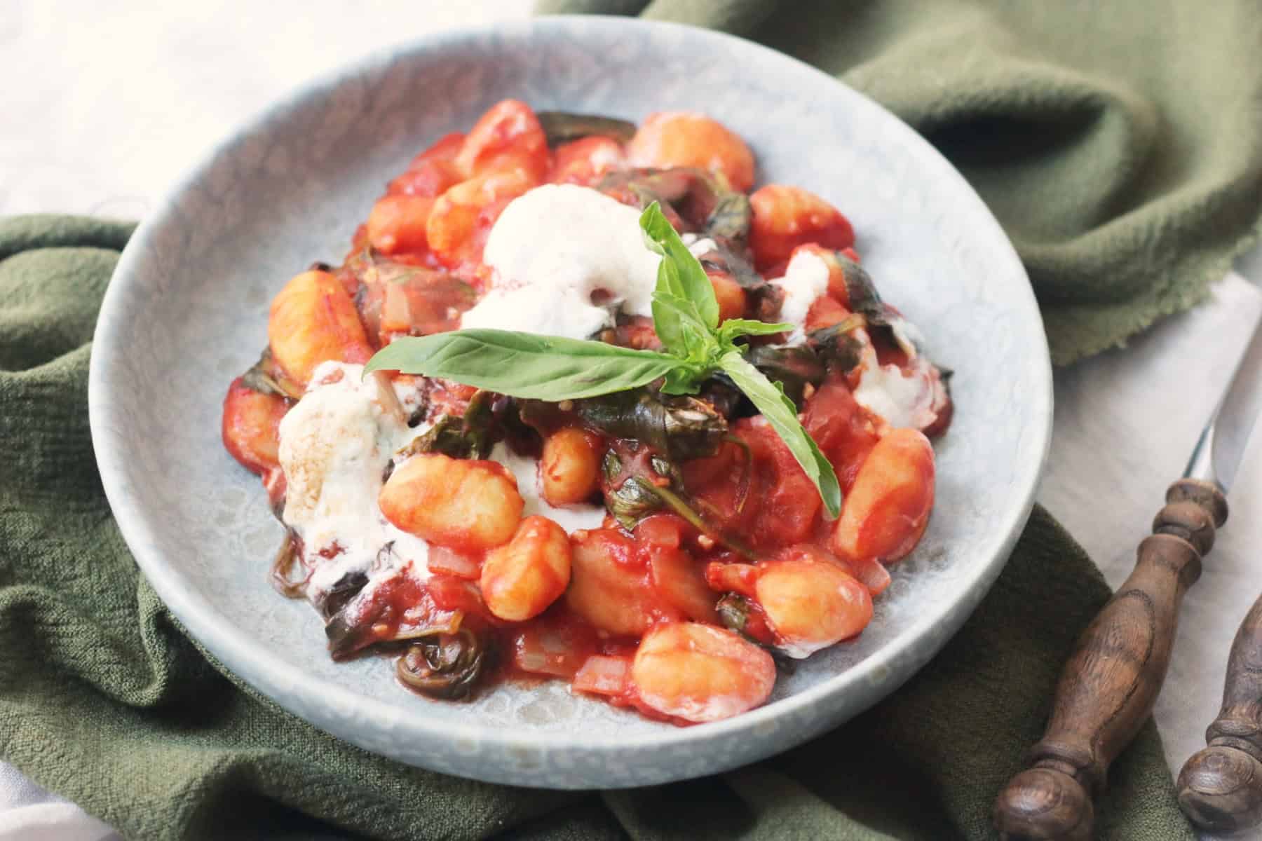 Vegan Baked Gnocchi topped with basil and served on a blue plate