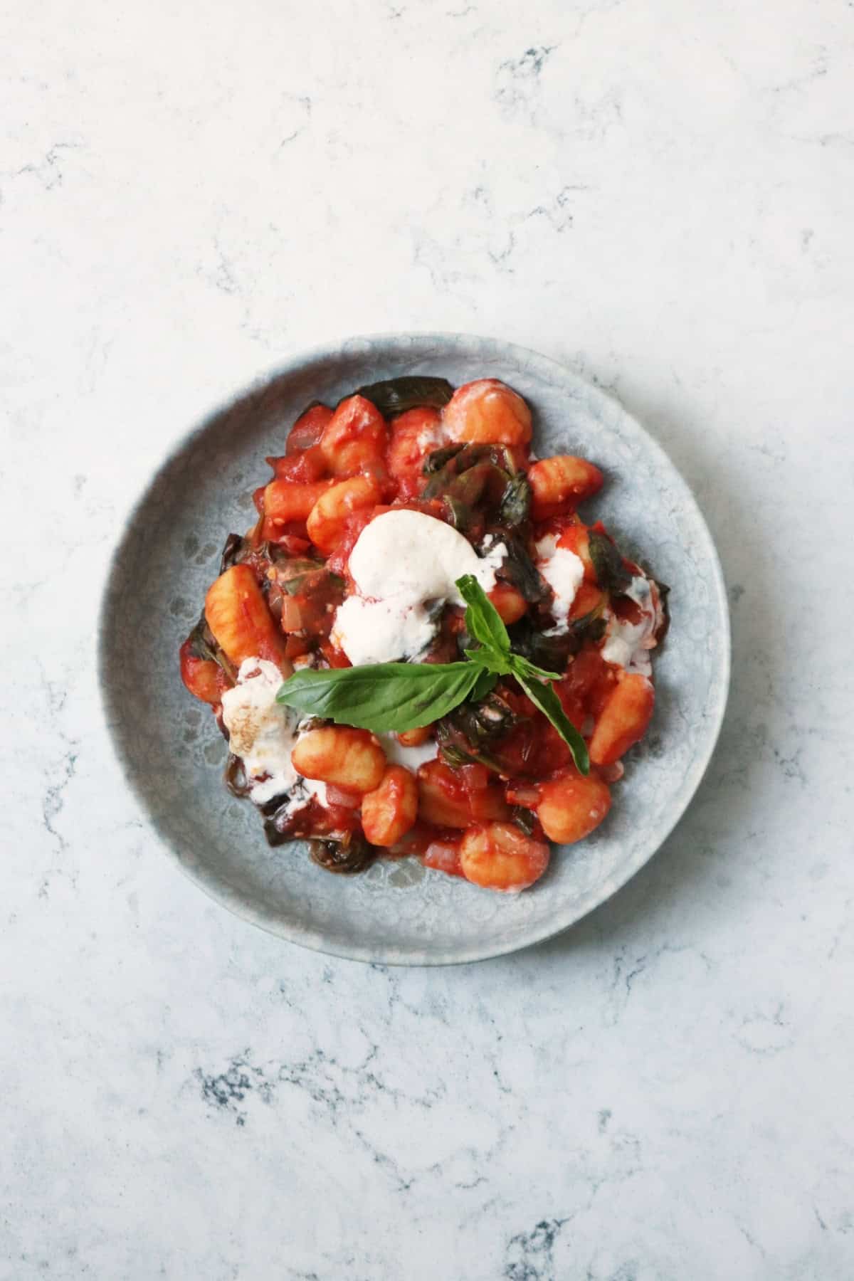 Vegan Baked Gnocchi topped with basil and served on a blue plate