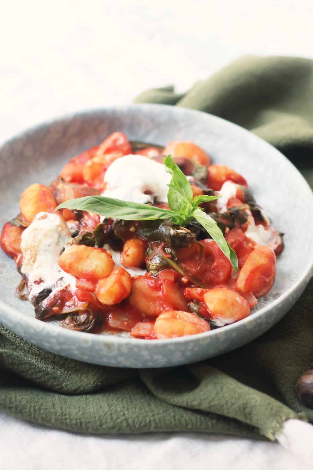 Vegan Baked Gnocchi topped with basil and served on a blue plate