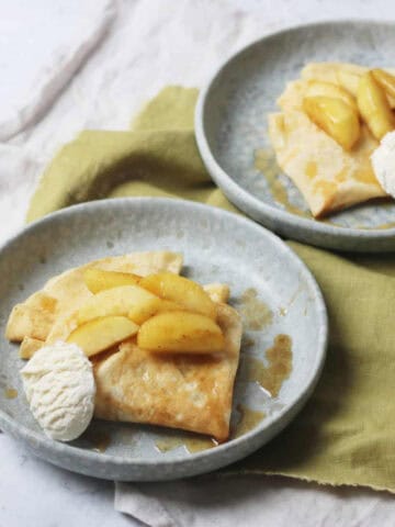 Two plates with vegan crêpe topped with caramelised apples and a scoop of vanilla ice cream