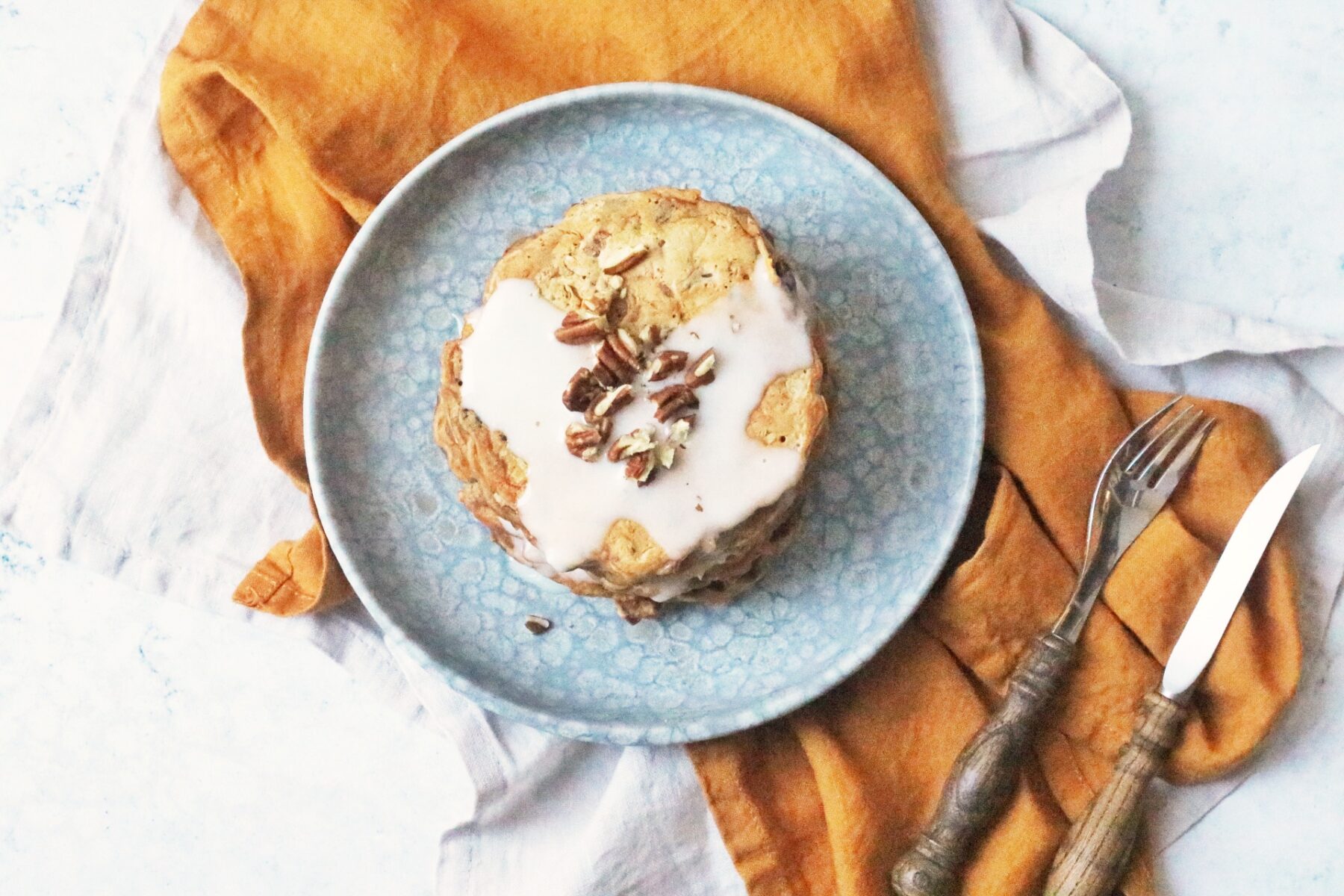 A stack of 6 vegan carrot cake pancakes topped with vegan cream cheese frosting and chopped pecan nuts.