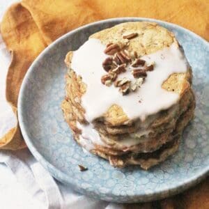 A stack of 6 vegan carrot cake pancakes topped with vegan cream cheese frosting and chopped pecan nuts.