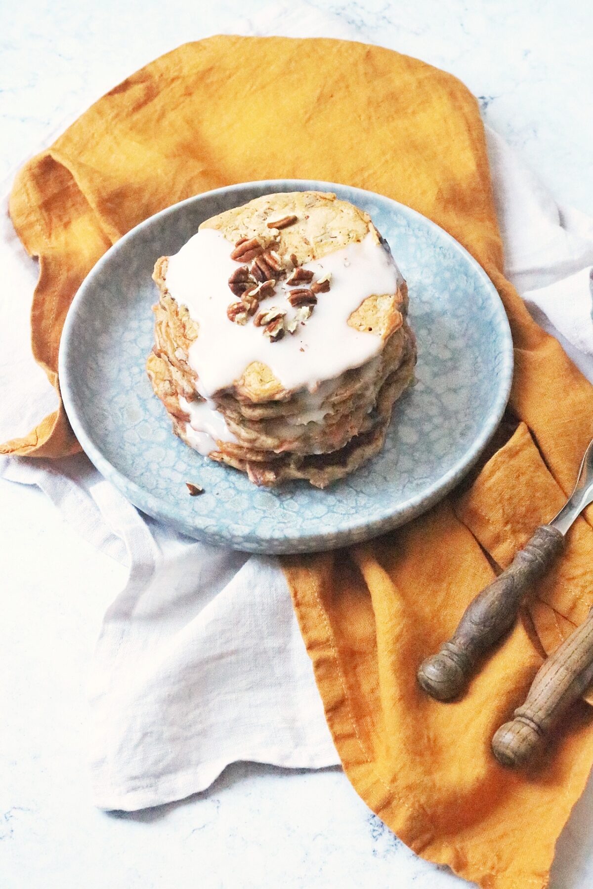 A stack of 6 vegan carrot cake pancakes topped with vegan cream cheese frosting and chopped pecan nuts.