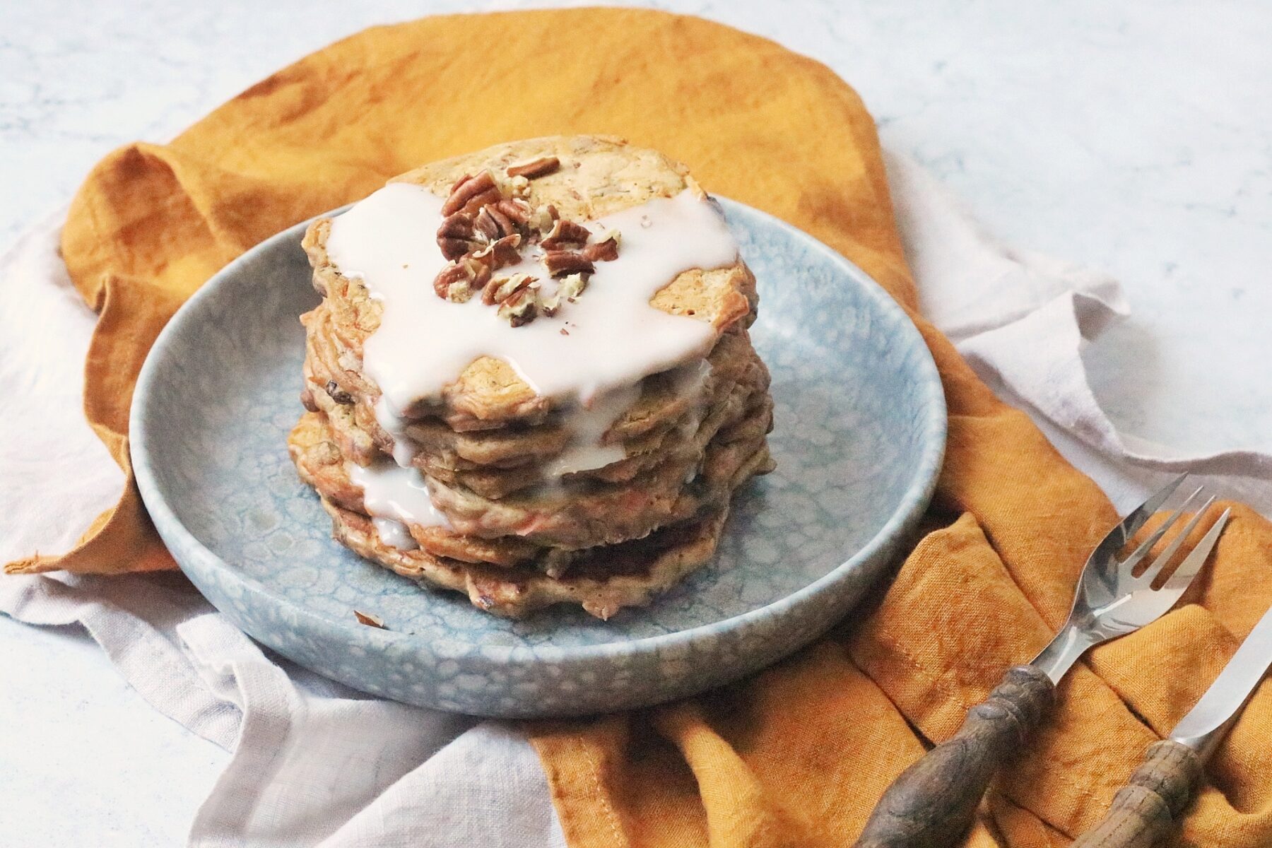 A stack of 6 vegan carrot cake pancakes topped with vegan cream cheese frosting and chopped pecan nuts.