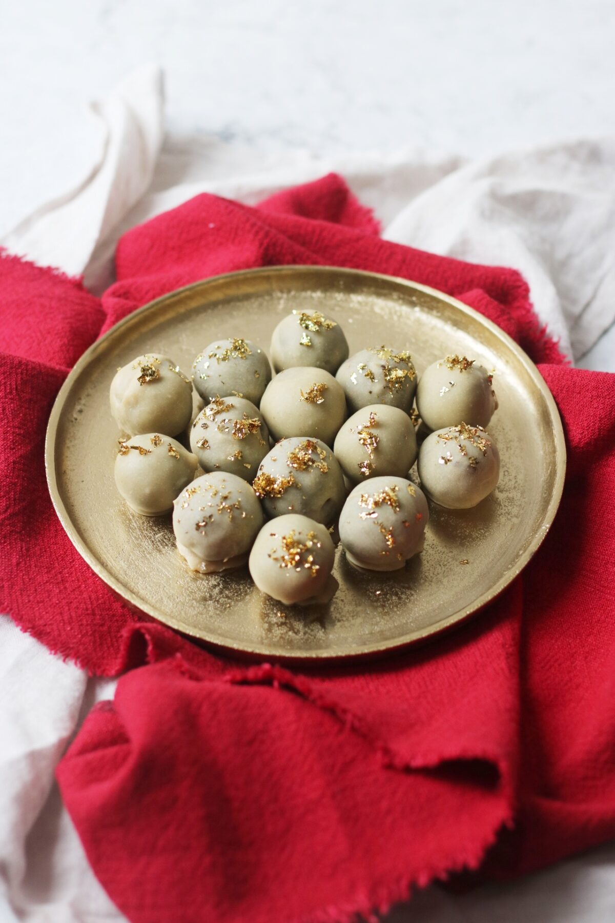 Vegan white chocolate and champagne truffles topped with gold leaf on a gold plate and red napkin.